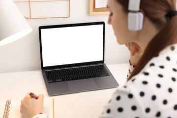 Wall Mural - E-learning. Woman taking notes during online lesson at table indoors, closeup