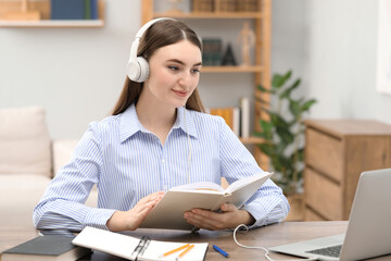 Wall Mural - E-learning. Young woman with book during online lesson at table indoors