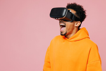 Wall Mural - Young man of African American ethnicity wear yellow hoody casual clothes watching in vr headset pc gadget open mouth isolated on plain pastel light pink background studio portrait. Lifestyle concept.