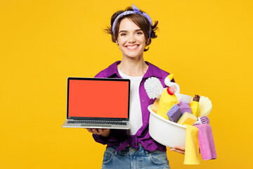 Canvas Print - Young IT woman wear purple shirt hold basin with detergent bottles do housework tidy up work use blank empty area screen laptop pc computer isolated on plain yellow background. Housekeeping concept.