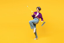 Full body young happy woman wears purple shirt casual clothes do housework tidy up hold in hand brush broom pov play guitar isolated on plain yellow background studio portrait. Housekeeping concept.