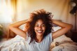 A joyful young woman with curly hair smiling brightly in a sunny bedroom, exuding happiness and comfort.