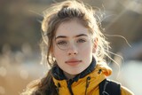 Fototapeta Paryż - A young woman is pictured wearing a bright yellow jacket and stylish glasses, walking along a riverside path on a sunny day in spring.