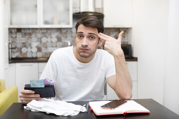 Wall Mural - Close up of unhappy man sitting at the table, stressed and confused by calculate expense from invoice or bills, have no money to pay mortgage or loan. High prices and spending money concept
