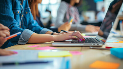 Wall Mural - close-up view of a person's hands working on a laptop with other individuals in the background, surr