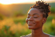 A beautiful young Black woman with natural hair stands outside with her eyes closed and a serene expression. She is surrounded by nature and the setting sun