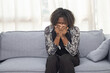 Black woman sitting on the couch whiles Sneezing  with tissue