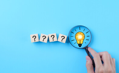 Idea discovery and inquiry concept. Hand holding a magnifying glass over question marks with light bulb, symbolizing idea discovery. Problem solving, Creative thinking, Company find business solution,