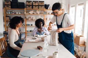 Multicultural pottery students sitting at pottery workshop with tutor.