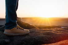 Closeup Of Feet Of Man In Special Boots Walking In The Mountains Reaching The Destination And On The Top Of Mountain At Sunrise Or Sunset. Travel Lifestyle Concept