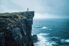 Person Standing At The Cliffs Overlooking The Ocean During A Storm