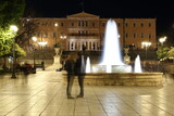 Fototapeta Paryż - Syntagma Square in Athens, night view, blurred people, fountain, building of Parliament 