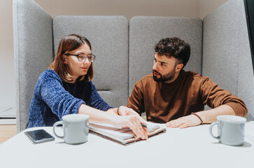 Wall Mural - Two focused people analyze documents during a collaborative effort at a modern workplace, with mugs and mobile phone on the table, depicting teamwork and problem-solving.