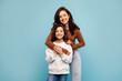 © Home-stock - Mother's love concept. Happy young mom posing with her preteen daughter from the back, standing on blue studio background, both smiling at camera