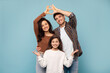 © Home-stock - Happy parents joining arms making fingers heart above their daughter, posing on blue studio background. Family and love concept