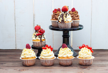 Wall Mural - Assorted beautiful vanilla cupcakes with fresh raspberry, strawberry, red currand on wooden background