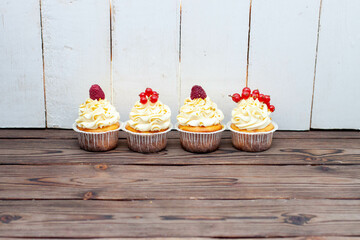 Wall Mural - Assorted beautiful vanilla cupcakes with fresh raspberry, strawberry, red currand on wooden background