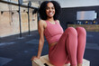 © Flamingo Images - A young black fit woman sits on a floor and smiles at the camera in pink sportswear