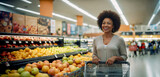 Fototapeta Konie - Beautiful middle-aged African American woman smiles while shopping at the supermarket with her cart in the fruit section.