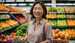 Beautiful middle-aged Japanese woman smiles while shopping at the supermarket with her cart in the fruit section.