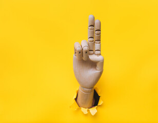 a wooden hand protrudes from a torn hole in yellow paper and shows two fingers. concept of catholici