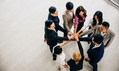 Wall Mural - From above, four diverse colleagues form a unity circle, holding hands to create a symbolic stack. This represents teamwork, trust, and global success in business.