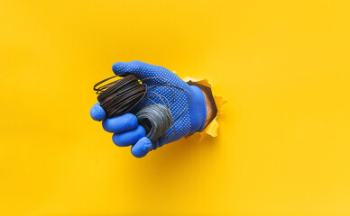 Wall Mural - A right man's hand in a blue knitted glove holds a two coil of steel wire. Torn hole in yellow paper. The concept of a worker, a labor migrant, a master of his craft. Copy space.