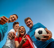 Bellow view, soccer fans with the ball cheering, blue sky background 