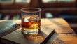 A glass of whiskey sits on a wooden table next to an open book