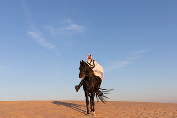 Wall Mural - Saudi man in traditional clothing in a desert riding his horse