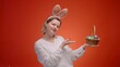 Woman in Easter bunny ears with a basket full of colored eggs on a red background, the concept of celebrating Easter and preparing for celebration