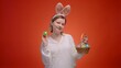 Woman in Easter bunny ears with a basket full of colored eggs on a red background, the concept of celebrating Easter and preparing for celebration