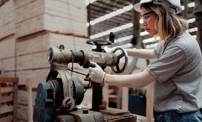 Confident female worker standing in lumber warehouse of hardwood furniture factory inspecting production machine. Serious technician woman, engineer busy working with tool in woodwork manufacturing.