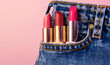 © alla.naumenco - In the pocket of the jeans there are some lipsticks. light red background.
