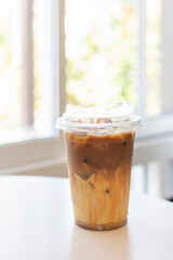 Take a way glass of iced caramel macchiato on white table.