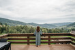 © Oleksandr - Young woman staying on terrace of wooden modern house with panoramic windows near pine forest. Concept of solitude and recreation on nature. Wellness and mindful resort. Beautiful place for vacation.