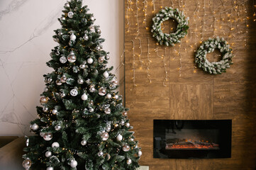 Wall Mural - Fir wreaths with lights on the wall with a fireplace and a Christmas tree, New Year decor