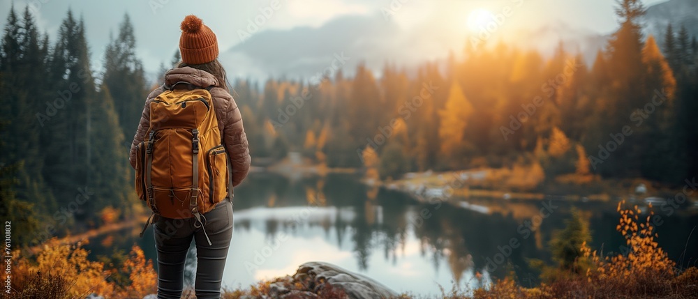 Adventurer in warm attire sits on a rock facing a peaceful mountain ...