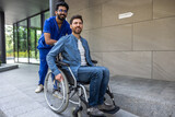 Fototapeta Młodzieżowe - Young dark-haired male nurse taking a patient in wheelchair for walk
