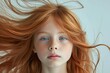 Beautiful young girl with red hair and blue eyes looking into the camera with her hair blowing in the wind
