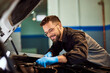 © bnenin - A smiling male mechanic technician checked a car under the opened hood, wearing protective gloves.