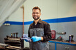 © bnenin - A smiling mechanic man posing for the camera, holding a tool for checking the oil in the car.