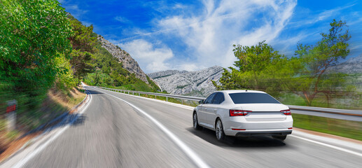 Wall Mural - A white car drives along the highway against the backdrop of rocky mountains on a sunny day.