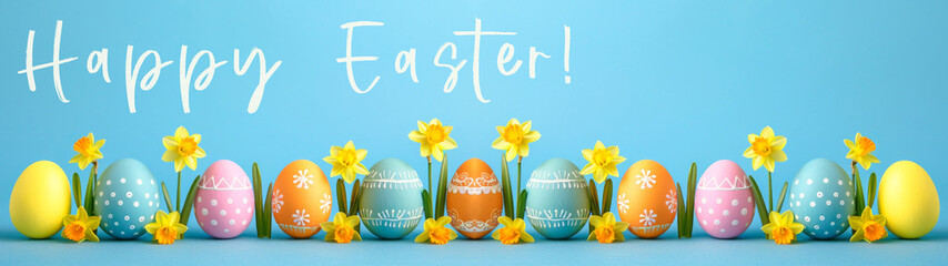 Wall Mural - Easter holiday celebration banner greeting card banner panorama long with text - Set collection of big colorful painted easter eggs and daffodils flowers on table with blue background