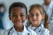 A photo of two happy kids in white coats with stethoscopes. One of the kids is an african american boy with short hair. He is standing in front of the other kid who is a caucacian girl