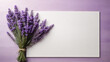 Bouquet of lavender flowers and white blank card on light purple wooden background.