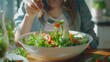 © Fotograf - A woman sitting at a table eating a salad. Perfect for healthy lifestyle concepts