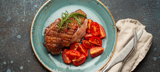 Wall Mural - Delicious roasted duck breast fillet with golden crispy skin, with pepper and rosemary, top view on ceramic blue plate served with cherry tomatoes salad, rustic concrete rustic background