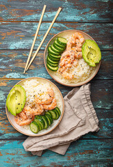 Canvas Print - Two white ceramic bowls with rice, shrimps, avocado, vegetables and sesame seeds and chopsticks on colourful rustic wooden background top view. Healthy asian style poke bowl.