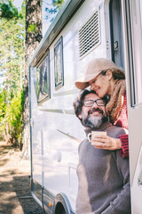 Wall Mural - Happy people on travel lifestyle sitting on the door of a camper van parking in the nature forest park. Enjoying vanlife couple. Renting vehicle for vacation and off grid independent house motorhome